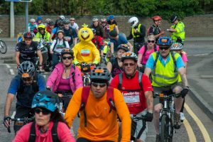 London to Brighton cycling event. Crowd of cyclists with yellow Big Bird character in the middle. Police giving cyclist ticket.